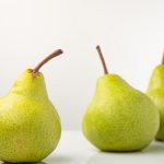 Three organic pears on a reflective white surface showcasing freshness and simplicity.